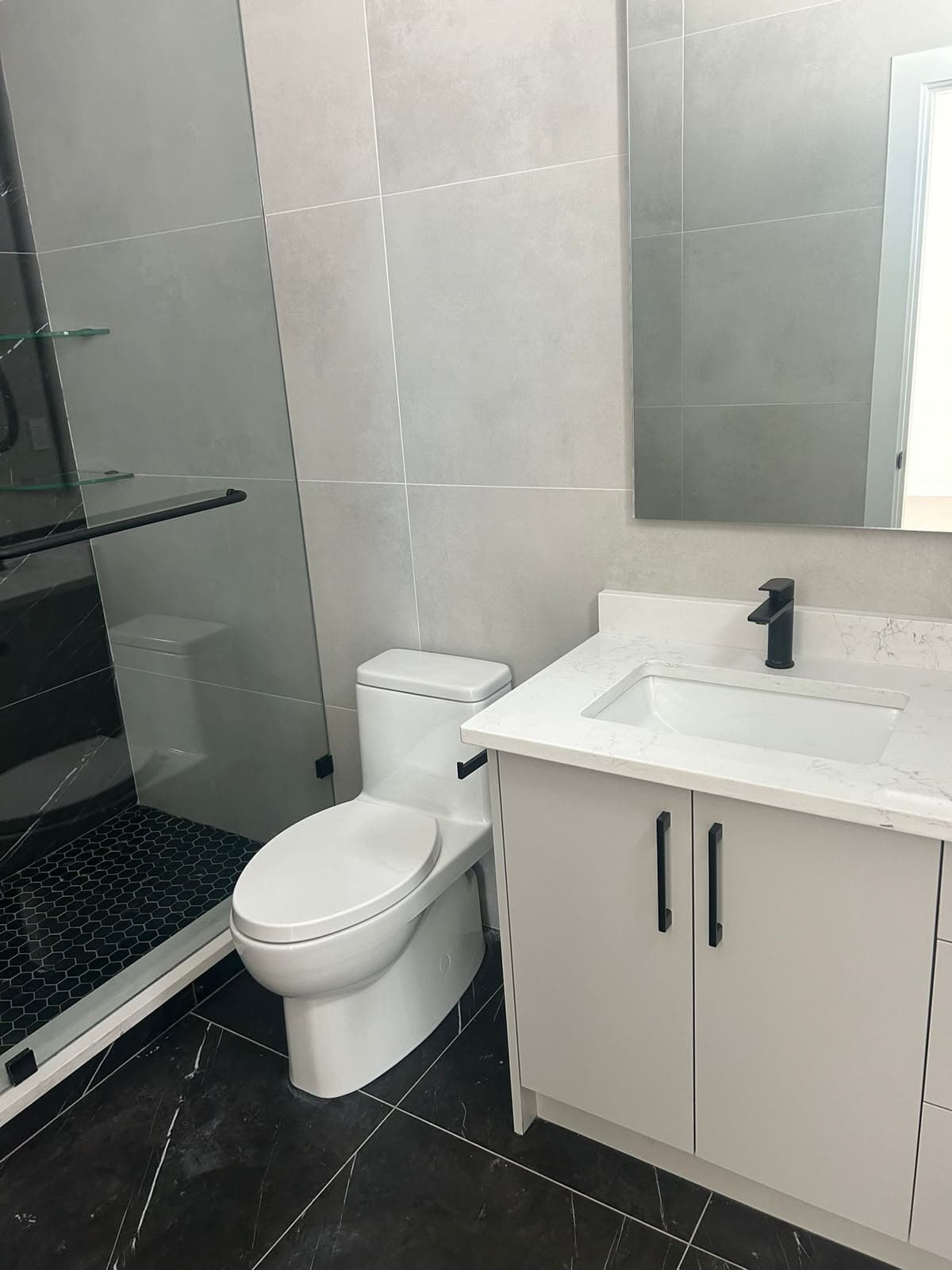 Bathroom with a one-piece toilet, vanity with matte black faucet and glass shower
