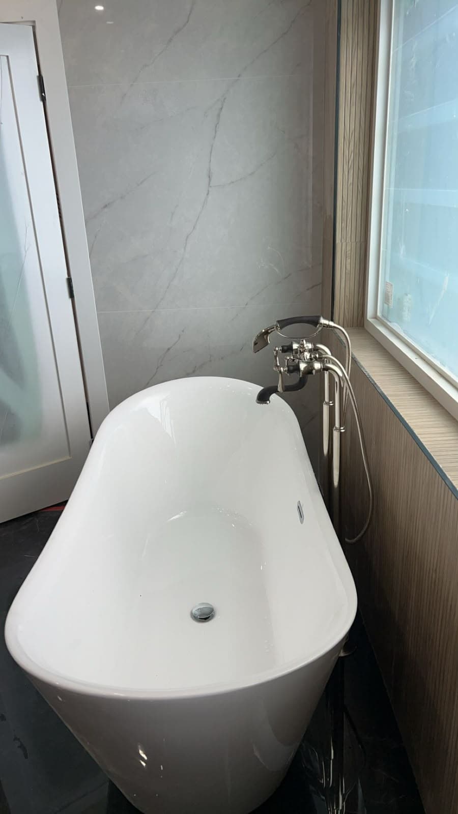 Freestanding bathtub with a floor-mounted filler and hand shower